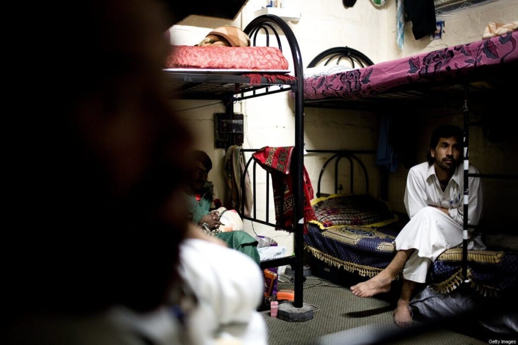عمال مهاجرون يجلسون على أسرّة بطابقين داخل معسكرات العمل في أبو ظبي
