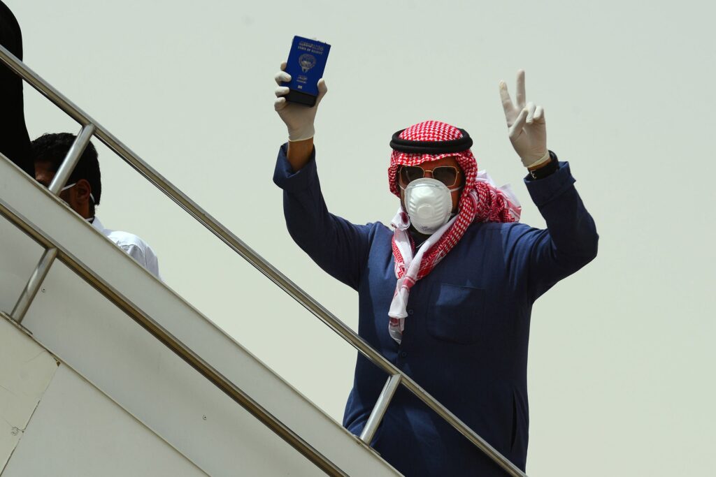 مواطن كويتي يرتدي قناعًا للوقاية من كورونا ويحمل جواز سفره أثناء صعودة على سلم طائرة